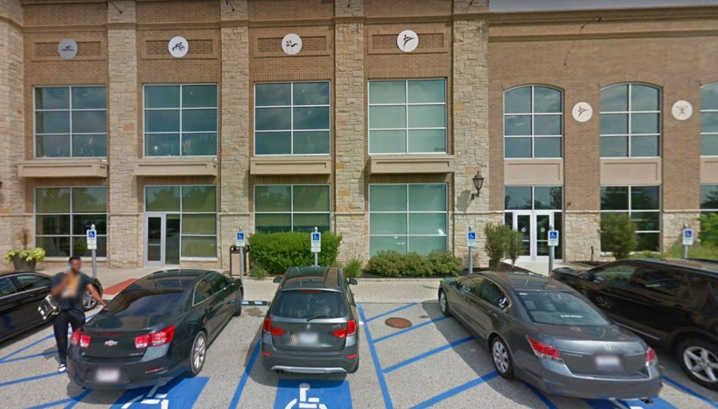 Three cars are parked in handicap spaces in front of a building with large windows and stone accents. Handicap signs are visible, and a person is walking toward the entrance, showcasing the quality work by Ohio Paving and Construction.