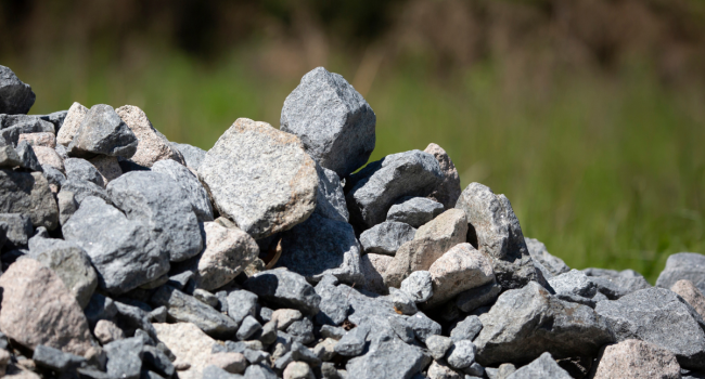 A pile of various-sized gray rocks and stones sits outdoors, hinting at materials ideal for ohio concrete recycling, with green grass and blurred vegetation in the background.